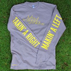 a gray long sleeve shirt with yellow lettering on the front and back, sitting in grass