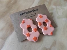 two pairs of pink and orange earrings sitting on top of a wooden table next to a card