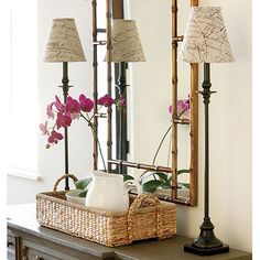 a table with a basket and two lamps on top of it next to a mirror