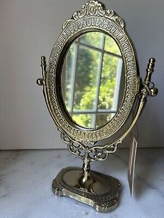 an antique style mirror on top of a stand with a window in the back ground