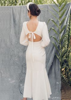 a woman standing in front of a wall wearing a white dress with open back and long sleeves