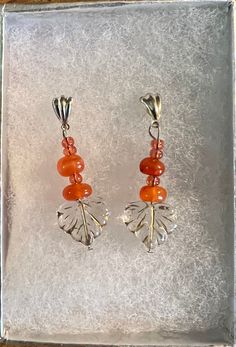 Amber brightens and welcomes the golden hues of fall! These earrings hold chunks of polished amber with tiny pale orange-pink glass seed beads, and clear gold embossed glass leaves, hung from silver posts. Orange Czech Glass Dangle Earrings, Amber Czech Glass Dangle Earrings, Amber Beaded Dangle Earrings, Handmade Orange Sterling Silver Earrings, Amber Beaded Drop Earrings For Gift, Handmade Sterling Silver Orange Earrings, Orange Carnelian Dangle Earrings, Handmade Orange Carnelian Earrings, Handmade Carnelian Orange Earrings