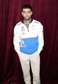 a man standing in front of a red curtain wearing white pants and a blue shirt