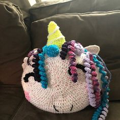 a crocheted unicorn hat sitting on top of a couch next to a pillow