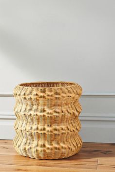 a wicker basket sitting on top of a hard wood floor next to a white wall