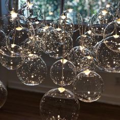 many clear glass balls are hanging from a chandelier with lights on them in front of a window