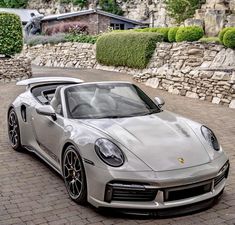 a silver porsche sports car parked in front of a stone wall and shrubbery behind it