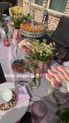 a table with plates and cups on it outside next to a brick building filled with flowers