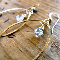 "A pair of sparkling white topaz briolettes is top wrapped in gold and framed by delicate 14k gold filled hoops. Each 14K gold filled hoop is hand shaped, forged, and polished to a glittering finish. Also available in rose gold and sterling silver. These earrings are in it for the long haul : we only use high quality 14k gold filled and rose gold filled, which will never wear off or change color no matter how much you wear them. The sterling silver version of these hoops are made from high quali Gold White Topaz Earrings For Gift, Gold White Topaz Earrings For Anniversary, Gold White Topaz Earrings For Wedding, Gold Jewelry With White Topaz Birthstone, Gold Teardrop Earrings With Gemstone For Anniversary, Topaz Jewelry November, November Birthstone Jewelry, White Topaz Earrings, Bar Jewelry