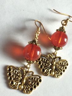 Rustic Butterfly Charm Earrings they are made with a beautiful detailed Butterfly Charm and Antique Spacers they are also having a Rust Tone Jade Style Translucent Bead they are 1.5” long Vintage Red Jewelry With Dangling Beads, Orange Beaded Vintage Earrings, Vintage Orange Beaded Earrings, Nickel-free Red Drop Earrings Jewelry, Red Czech Glass Beaded Earrings With Dangling Beads, Red Pierced Drop Earrings, Elegant Red Czech Glass Earrings, Amber Beaded Dangle Earrings, Red Beaded Czech Glass Earrings