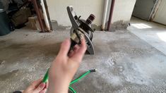 a person holding a green hose in front of a metal object on concrete flooring