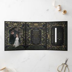 an open black and gold wedding program booklet on a marble table with scissors, flowers and other items