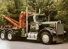 a green and orange truck is parked in front of some trees