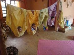 two children are sitting in hammocks with yellow drapes hanging from the ceiling