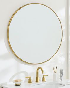 a bathroom with a round mirror above the sink and gold faucets on the counter