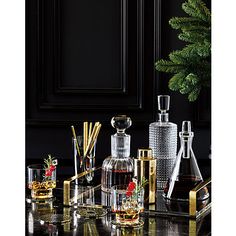 a table topped with bottles and glasses filled with liquor next to a christmas tree in a black room