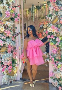 a woman wearing a pink dress standing in front of a flower covered doorway with flowers all around her