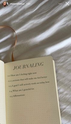 an open book sitting on top of a bed next to a white sheet with writing