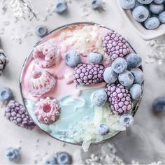 a bowl filled with blueberries and whipped cream on top of a table next to berries