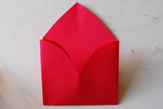 an origami envelope is folded in red paper and placed on a white surface