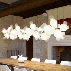 a dining room table with white chairs and lights hanging from the ceiling