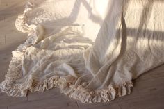 an unmade bed with white sheets and ruffles on the floor in front of a window