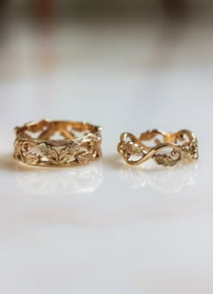 two gold rings sitting on top of a white counter next to each other and one has an intricate design