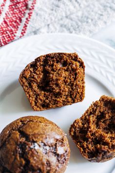 three chocolate muffins on a white plate next to a red and white towel