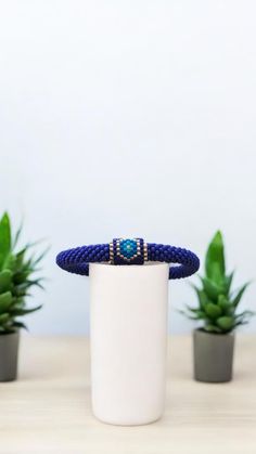 a blue beaded bracelet sitting on top of a white cup next to potted plants