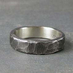 a silver ring with a textured surface on the outside and inside, sitting on a gray surface