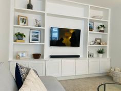 a flat screen tv mounted to a wall in a living room with white shelving