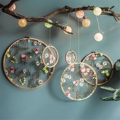 three plates hanging from a branch with flowers on them and some lights in the background