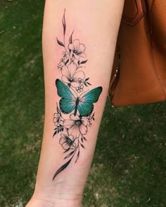 a woman's arm with a blue butterfly and flowers tattoo on the left forearm