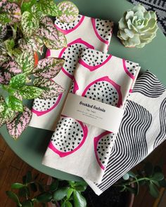 two napkins with pink and black designs on them sitting next to a potted plant