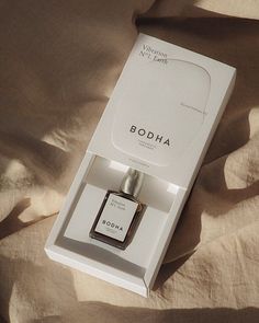 a bottle of bodha perfume sitting in a white box on top of a bed