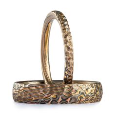 "These hand-crafted Mokume Gane bands are shown in the Twist pattern and the Oxidized Firestorm metal combination, with a low dome profile and etched and oxidized finish. Firestorm features 14k red gold, 14k yellow gold, Palladium, and sterling silver. These rings also both have a hammered finish effect for some added texture and visual interest. Mokume Gane Band - Ring 1 Pattern: Twist Palette: Firestorm Width: 2mm Size Shown: 10 Profile: Low Dome Finish: Etched & Oxidized Additional Option Artisan Engraved Rings For Promise, Heirloom Hand Forged Round Band Rings, Heirloom Thick Band Gift Bands, Heirloom Thick Band Gift, Artisan Adjustable Yellow Gold Ring, Artisan Promise Ring, Handmade Heirloom Ceremonial Ring, Hand Forged Adjustable Round Band Ring, Adjustable Hand Forged Round Band Ring