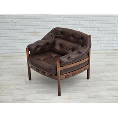 a brown leather chair sitting on top of a wooden floor next to a brick wall