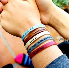 two hands holding onto each other with different bracelets on their wrists and the words love written on them