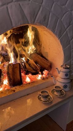 a fire is burning in an oven with tea cups on the counter next to it