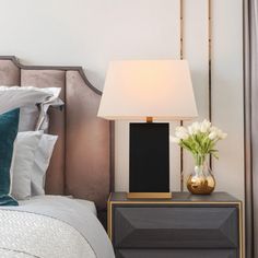 a nightstand with a lamp on top of it next to a bed in a bedroom