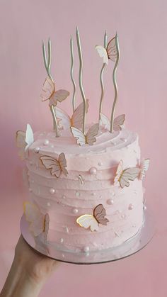 a pink cake with butterflies on it being held by a woman's hand in front of a pink background