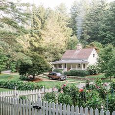 a car parked in front of a white picket fence with flowers and trees around it