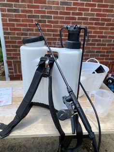 an image of a sprayer and water jugs on a picnic table with brick wall in the background