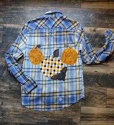 Happy fall ya'll.  Get festive and stay cozy in this women's size medium flannel shirt.  Blue and dark yellow plaid flannel has been lightly bleached in the middle section.  Three adorable, small pumpkins can be found on the front left breast. One pumpkin is a black fabric with beautiful large sunflowers. The other two patches are orange, black, and white checkered pattern.   3 pumpkin patches can also be found on the back of the card. The larger middle pumpkin is made out of that same orange, b Fall Cotton Fitted Shirt, Fitted Cotton Shirt For Fall, Plaid Relaxed Fit Shirt For Fall, Fitted Plaid Shirt For Fall, Relaxed Fit Plaid Shirt For Fall, Fall Plaid Flannel Tops, Fall Cotton Shirt In Orange, Fall Graphic Print Long Sleeve Flannel Shirt, Fall Long Sleeve Flannel Shirt With Graphic Print