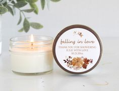 a white candle sitting next to a glass jar with a label that says falling in love