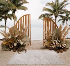 an outdoor ceremony setup with palm trees and flowers on the sand near the water's edge