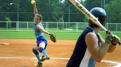 two women playing softball on a baseball field, one throwing the ball to the other