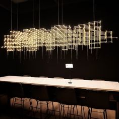 a long table with chairs and lights hanging from it's sides in front of a black wall