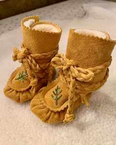 a pair of brown baby shoes with green embroidered leaves on them sitting on a white carpet