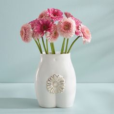 a white vase filled with pink flowers on top of a table